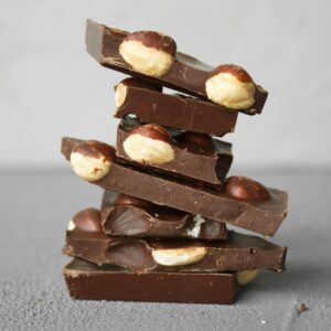 A stack of dark chocolate bars filled with whole nuts on a textured gray background.