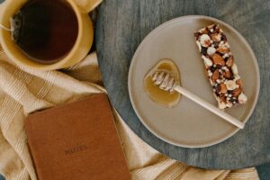 Top view of a nut bar snack, honey dipper, and tea on a wooden table with a notebook.